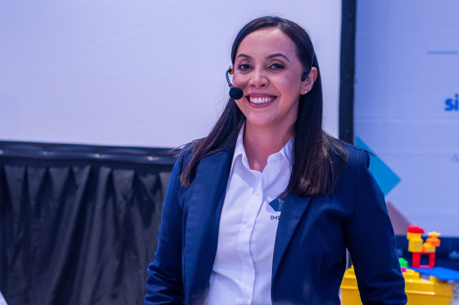 Perla Torres hablando en un escenario, con micrófono de diadema